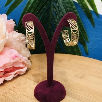 Brincos dourados em suporte de veludo roxo com flores e folhas ao fundo