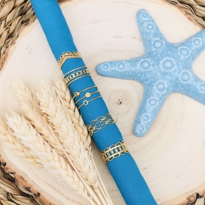 Pulseiras douradas finas sobre suporte azul com espigas de trigo e estrela do mar azul