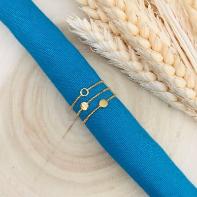 Três pulseiras douradas sobre pano azul com espigas secas ao lado