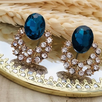 Brincos azul e pedras transparentes num espelho redondo com moldura dourada