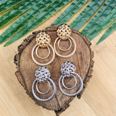 Dois pares de brincos dourados e prateados com aros trançados sobre fatia de madeira e folhas verdes