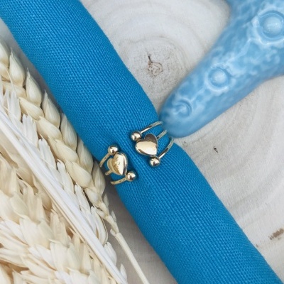 Anéis dourados com coração sobre pano azul em madeira clara com decoração de estrela do mar e trigo.