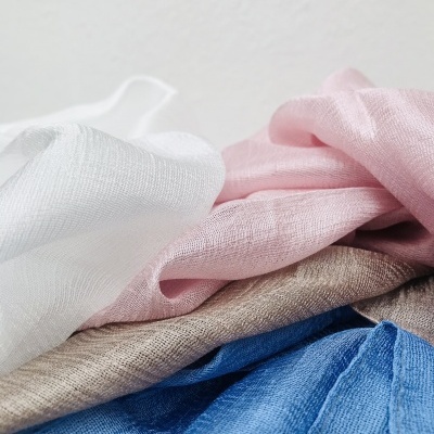 Tecidos finos em branco, rosa, bege e azul dispostos em camadas onduladas com fundo claro.