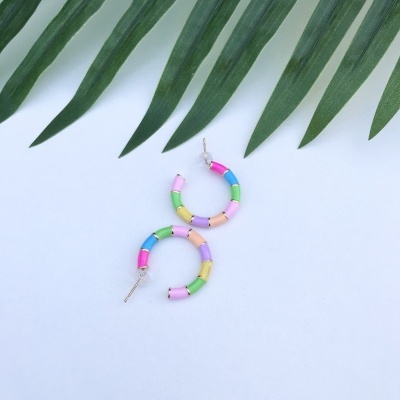 Brincos coloridos em forma de argola sobre fundo branco com folhas verdes