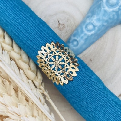 Guardanapo azul com anel dourado com padrão floral sobre mesa de madeira clara com decoração azul e palha