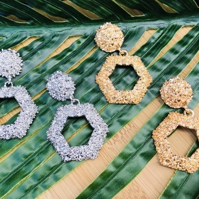 Brincos hexagonais texturizados prateado e dourado sobre folha verde
