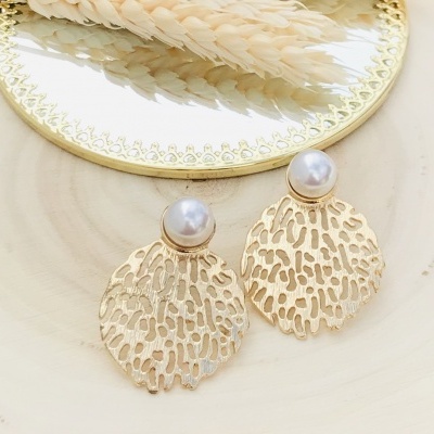 Brincos dourados com pérola branca sobre prato espelhado e superfície clara