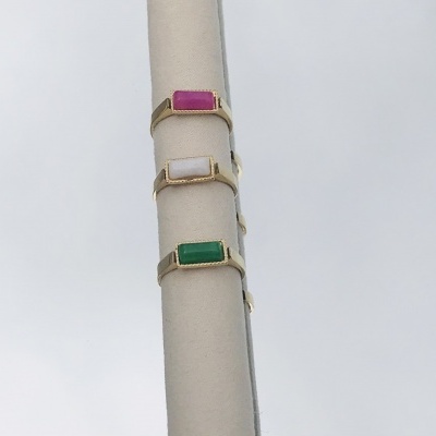 Três anéis dourados com pedras coloridas em suporte cilíndrico creme