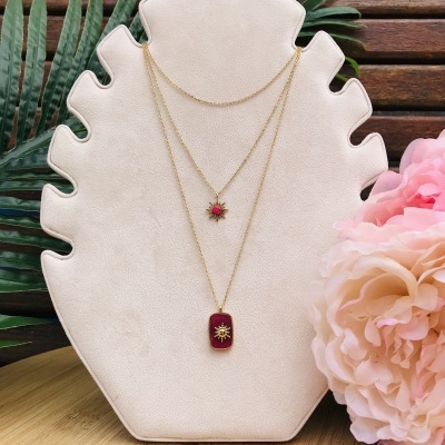 Colar duplo dourado com pendentes vermelhos exibido em suporte branco em forma de folha