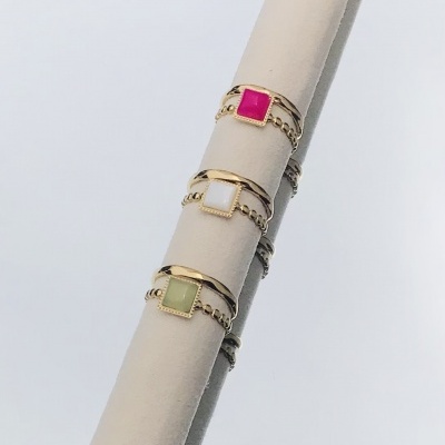 Três anéis dourados com pedras quadradas rosa, branco e verde num suporte bege