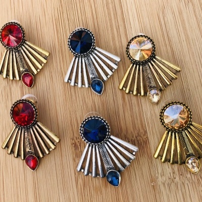 Brincos coloridos com pedras e elementos metálicos sobre madeira clara