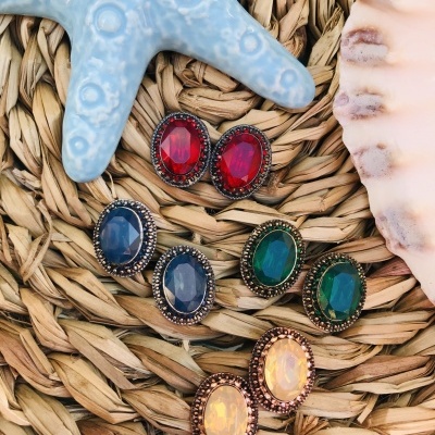 Quatro pares de brincos ovais coloridos sobre base de fibras naturais com estrela-do-mar azul e concha rosa