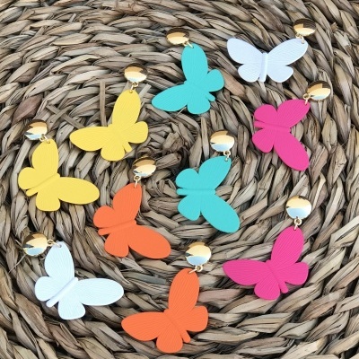Brincos coloridos de borboleta com fecho dourado sobre superfície trançada.