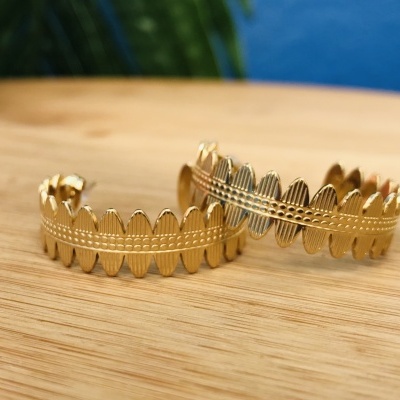 Duas pulseiras douradas com padrão de folhas sobre madeira clara