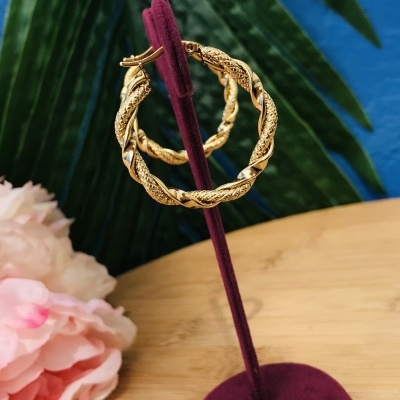 Brincos argola dourados texturizados expostos em suporte de veludo vermelho em fundo colorido