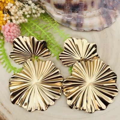 Brincos dourados em forma de folhas com relevo em fundo claro com flores e concha