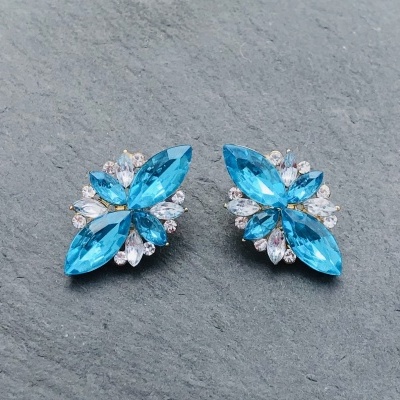 Par de brincos com pedras azuis e brancas sobre superfície cinza rugosa