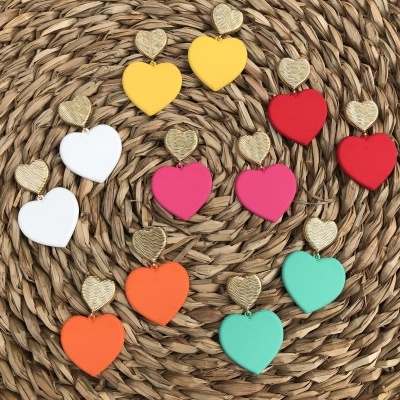 Brincos coloridos em forma de corações com detalhes dourados sobre superfície trançada