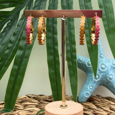 Brincos de argola dourados com corações coloridos pendurados em suporte