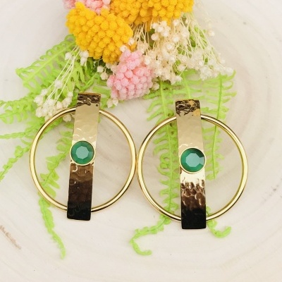 Brincos dourados com pedras verdes e aro circular, sobre base branca com flores decorativas