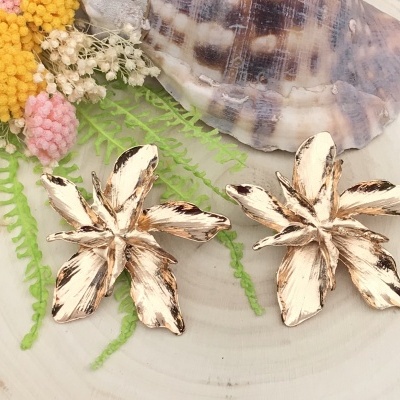 Brincos em forma de flores douradas envelhecidas com decoração natural ao fundo