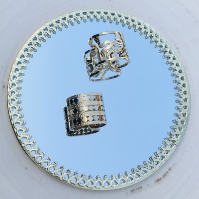 Anel prateado com padrão recortado sobre espelho redondo com moldura decorativa