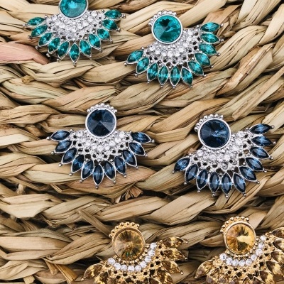 Brincos coloridos com pedras e detalhes metálicos sobre superfície de fibra natural