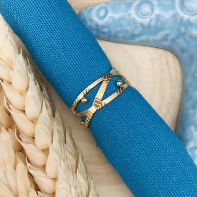 Guardanapo azul com anel dourado ao lado de espigas secas e estrela do mar azul clara.