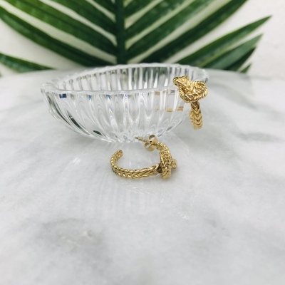 Brincos dourados com textura entrelaçada em prato de vidro transparente