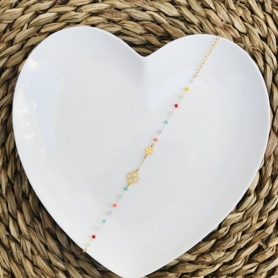 Pulseira dourada com contas coloridas sobre prato branco em forma de coração