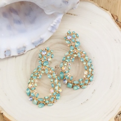 Brincos dourados com pedras turquesa em base de madeira com concha ao lado