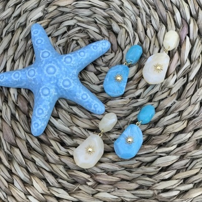 Brincos coloridos pendurados sobre superfície de fibra natural ao lado de uma estrela do mar azul