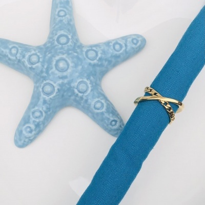 Anel dourado entrelaçado sobre tecido azul próximo a estrela-do-mar azul clara