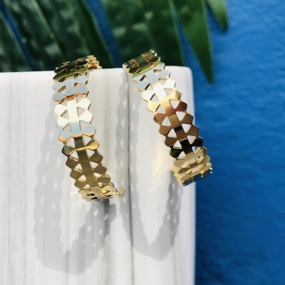 Brincos de argola dourados cortados em padrão recortado pendurados num suporte branco