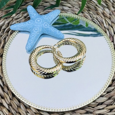 Brincos de argola dourados com textura torcional sobre espelho redondo com moldura dourada e decoração de estrela-do-mar azul.