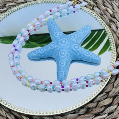Colar de contas transparentes e coloridas com estrela do mar azul em espelho redondo