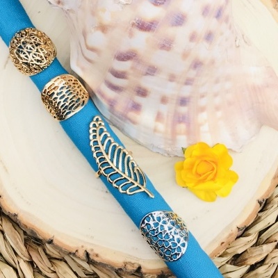 Guardanapo azul com argolas metálicas prateadas, concha grande e flor amarela sobre madeira