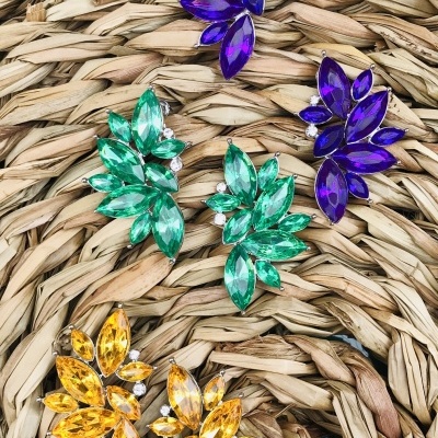 Brincos coloridos com pedras em forma de folhas sobre fundo de fibra entrelaçada