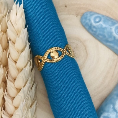 Anel dourado decorativo num tecido azul com espigas de trigo e cerâmica azul.