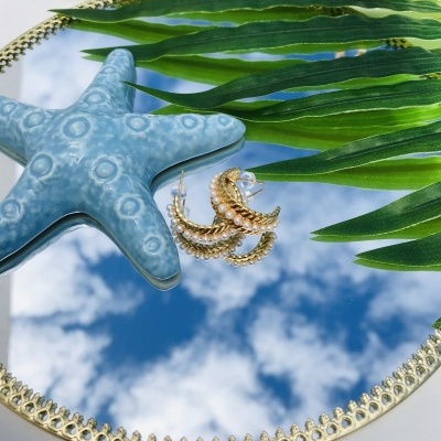 Espelho redondo dourado com reflexo do céu, estrela do mar azul e brincos dourados