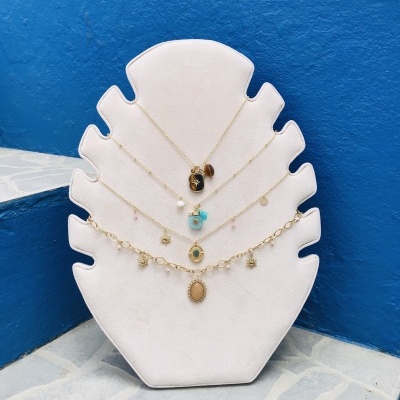 Cinco colares dourados com diferentes pendentes expostos em suporte branco em formato de folha.