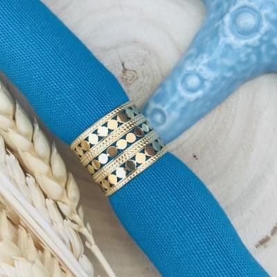 Guardanapo azul com argola decorativa dourada em base de madeira clara com ervas secas e objeto azul