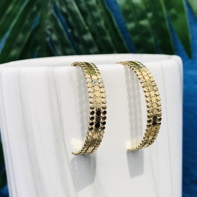 Brincos de argola dourados com padrão em relevo pendurados numa base branca