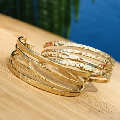 Brincos de argola dourados com textura martelada sobre madeira clara e fundo de piscina azul