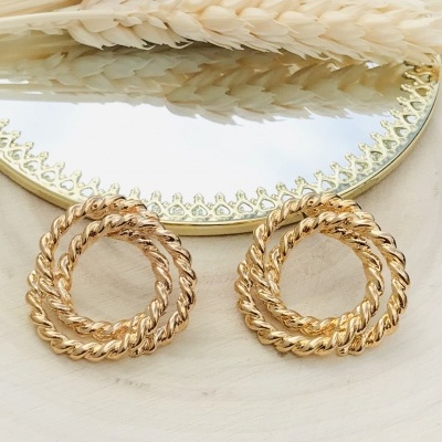 Brincos dourados trançados em círculo sobre base de madeira com espelho e espigas secas