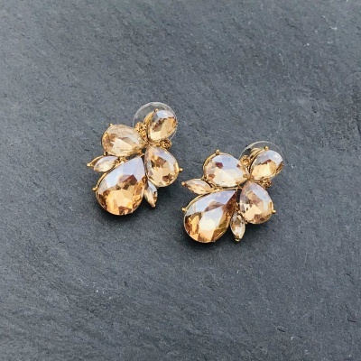 Brincos dourados com pedras âmbar sobre superfície de pedra cinza.