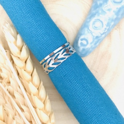 Anel prateado com design de folhas em tecido azul, espigas de trigo e concha azul clara ao fundo