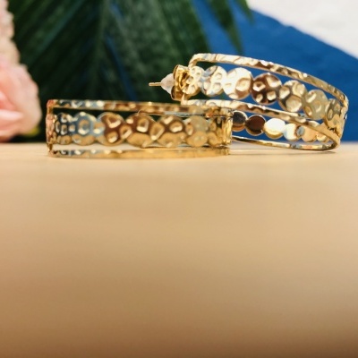 Par de brincos de argola texturizados dourados sobre superfície bege