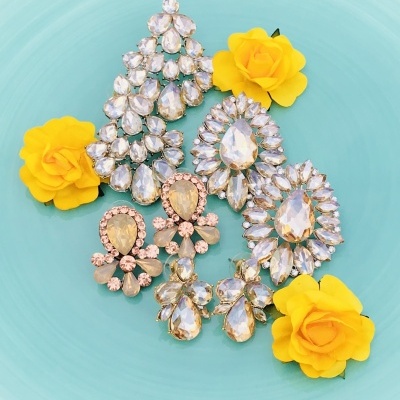 Quatro pares de brincos com pedras transparentes e douradas em prato azul com flores amarelas