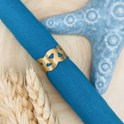 Guardanapo azul com anel dourado, estrela do mar azul e espigas claras sobre madeira clara